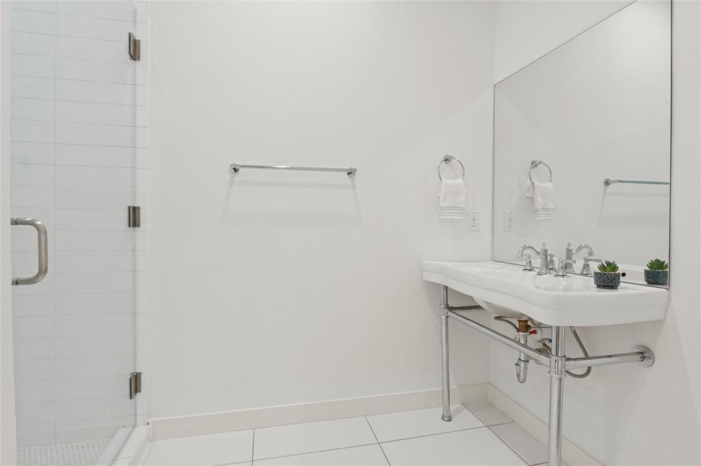 Wall-mounted console sink with chrome finish legs and widespread faucet, glass-enclosed shower with horizontal wall tile, and large-format floor tile