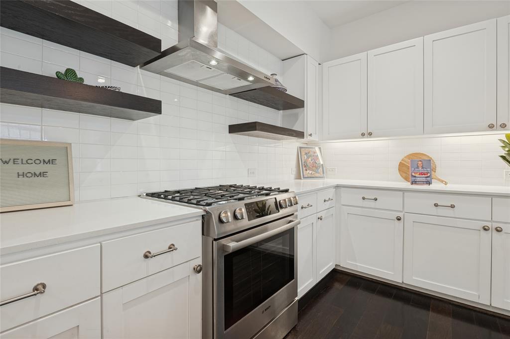 Kitchen featuring white shaker-style cabinetry, quartz countertops, stainless steel gas range, subway tile backsplash, and dark wood floating shelves