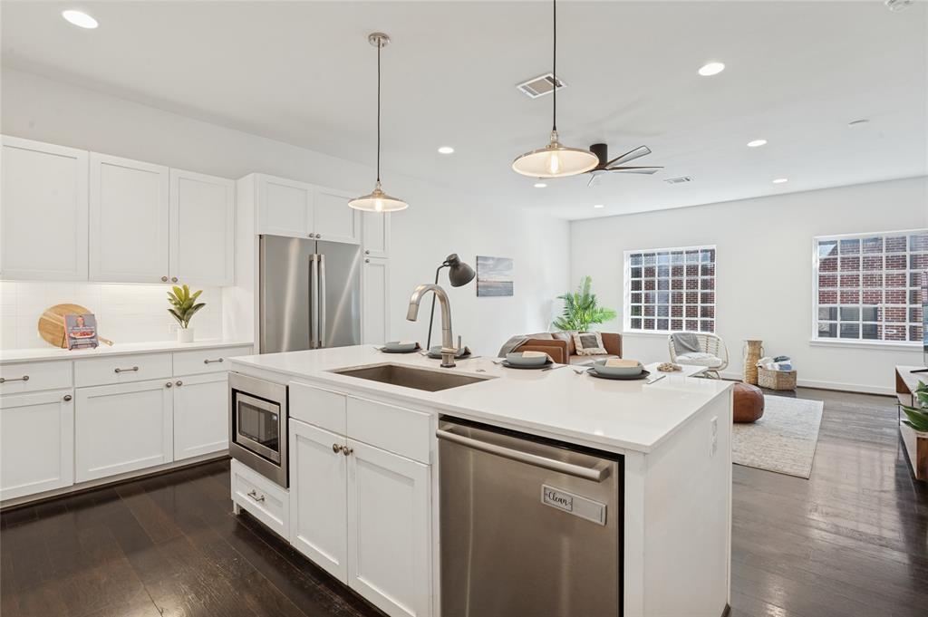 Kitchen featuring white shaker-style cabinetry, quartz countertops, a stainless steel undermount sink, pendant lighting, and wood-finish flooring