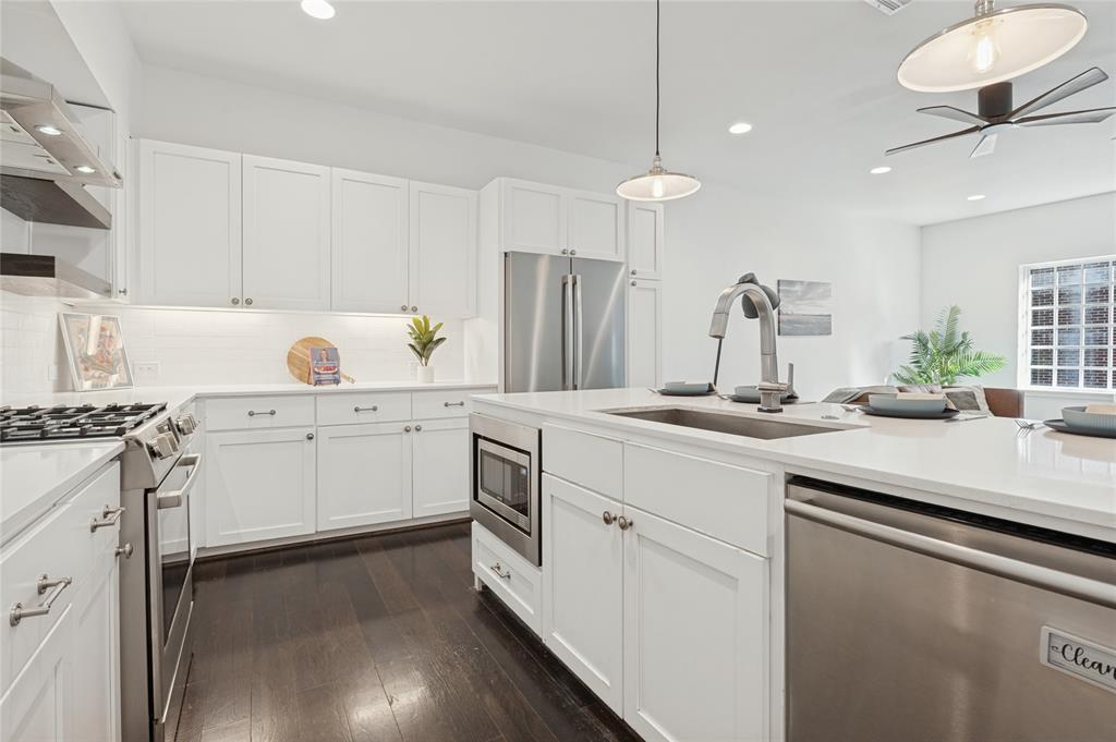 Kitchen featuring white shaker-style cabinetry, quartz countertops, stainless steel appliances, a central island with a built-in microwave, and wood-finish flooring