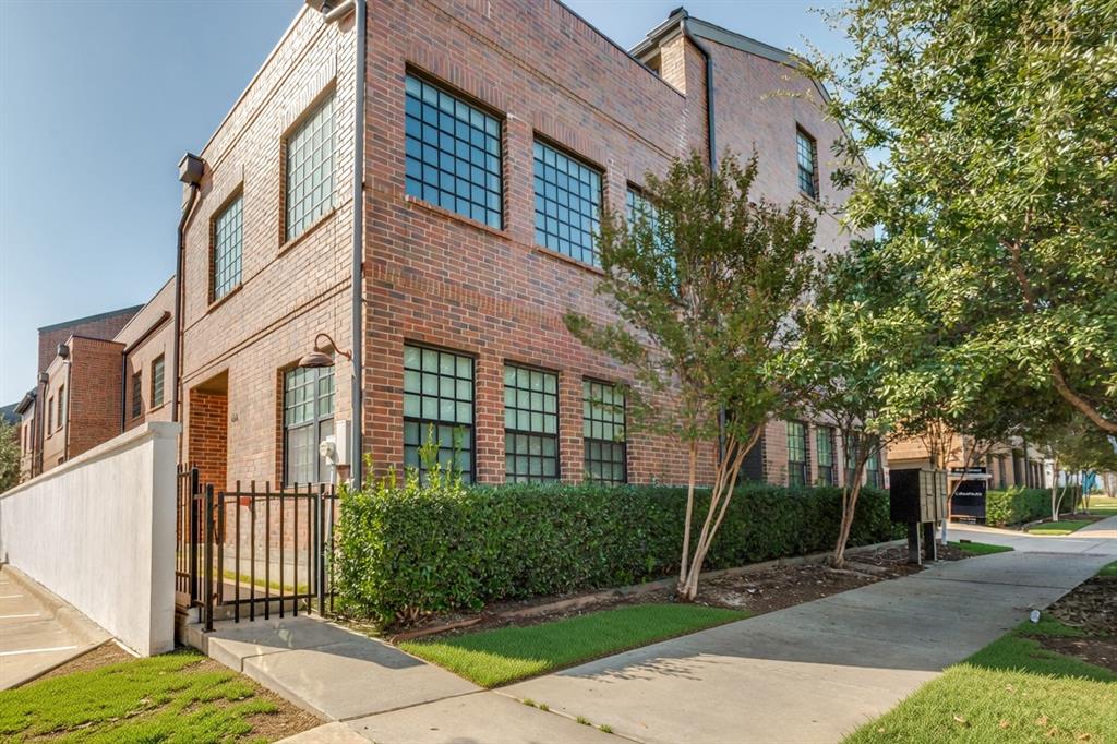 Multi-story brick exterior featuring grid-pattern windows, a gated entrance, and a white privacy wall