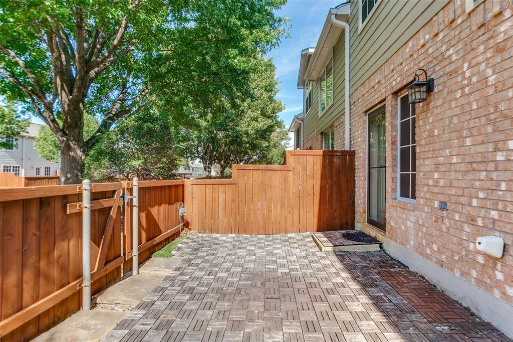 Patio area featuring interlocking pavers, enclosed by a full-height wood privacy fence with a gated entry, exterior wall-mounted lighting, and brick and horizontal siding exterior