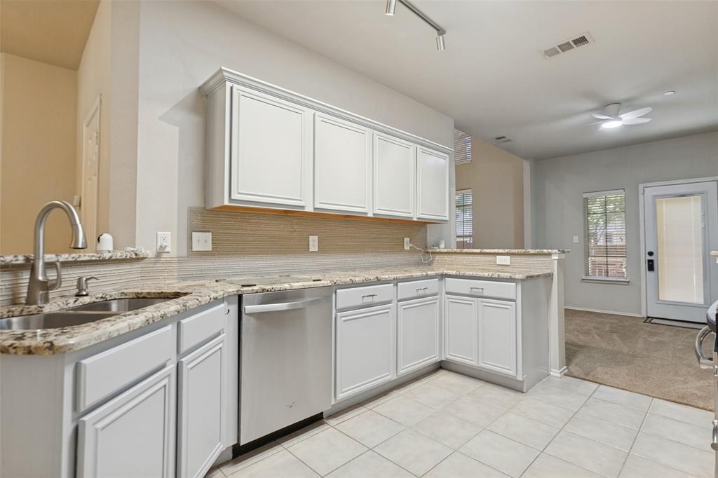 Kitchen featuring white shaker-style cabinetry, neutral stone-patterned countertops, a stainless steel undermount double-basin sink with a gooseneck faucet, light-toned tiled flooring, and integrated stainless steel dishwasher