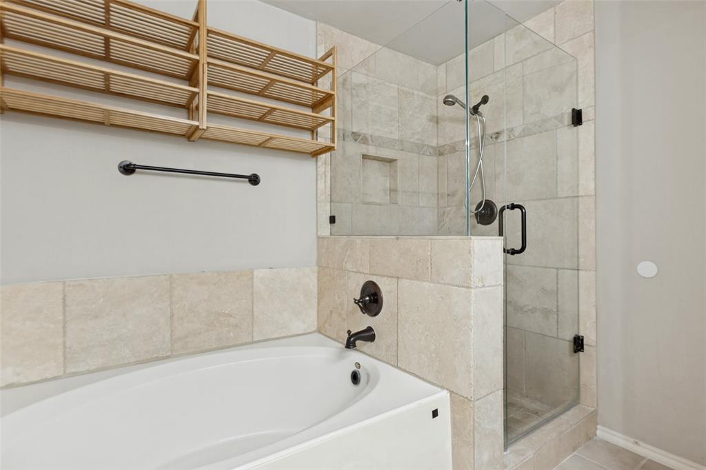 Deep soaking tub, walk-in shower with stone tile surround, glass enclosure, and matte black fixtures