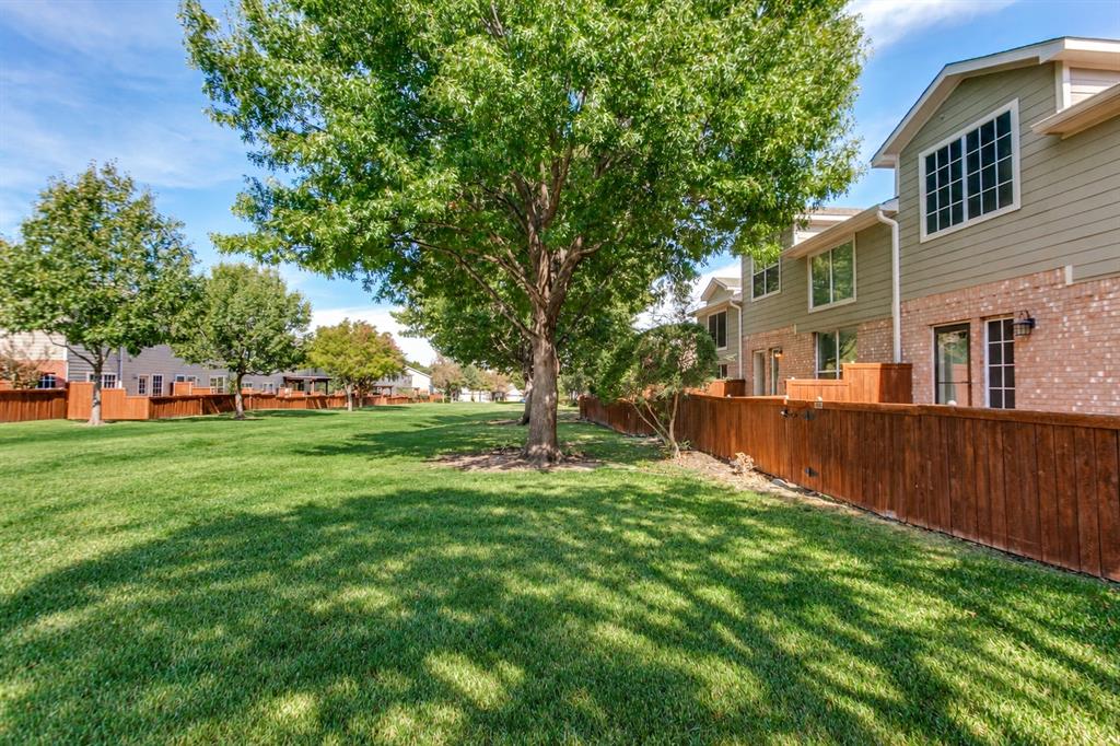 Expansive green space featuring mature trees and wood privacy fencing, complemented by a multi-story exterior with horizontal siding and brick masonry