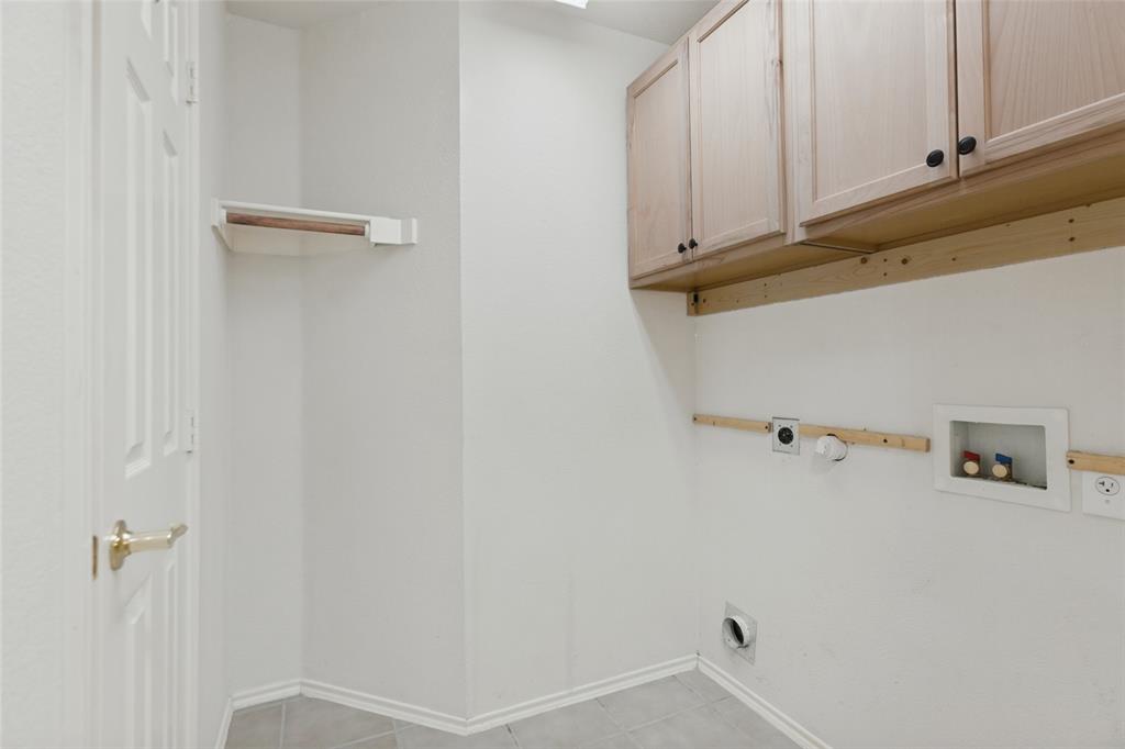 Utility space featuring wood-finish wall-mounted cabinetry, a built-in shelving unit, tile flooring, and dedicated hookups for laundry appliances