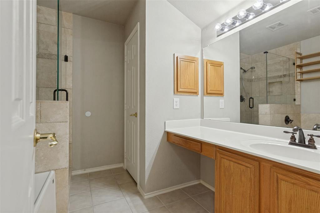 Bathroom featuring a vanity with a white countertop and oval under-mount sink, wood-finish cabinetry, a large wall-to-wall mirror, and a glass-enclosed shower with tiled walls