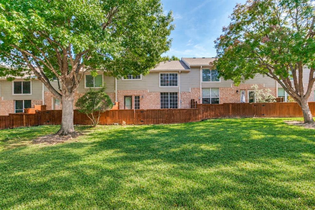 Exterior facade featuring mixed brick and siding, a wood privacy fence, and mature shade trees situated on a grassy lawn