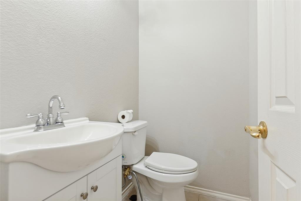 White vanity featuring a drop-in sink, chrome two-handle faucet, and built-in cabinet storage paired with a white toilet and a door with brass-tone hardware