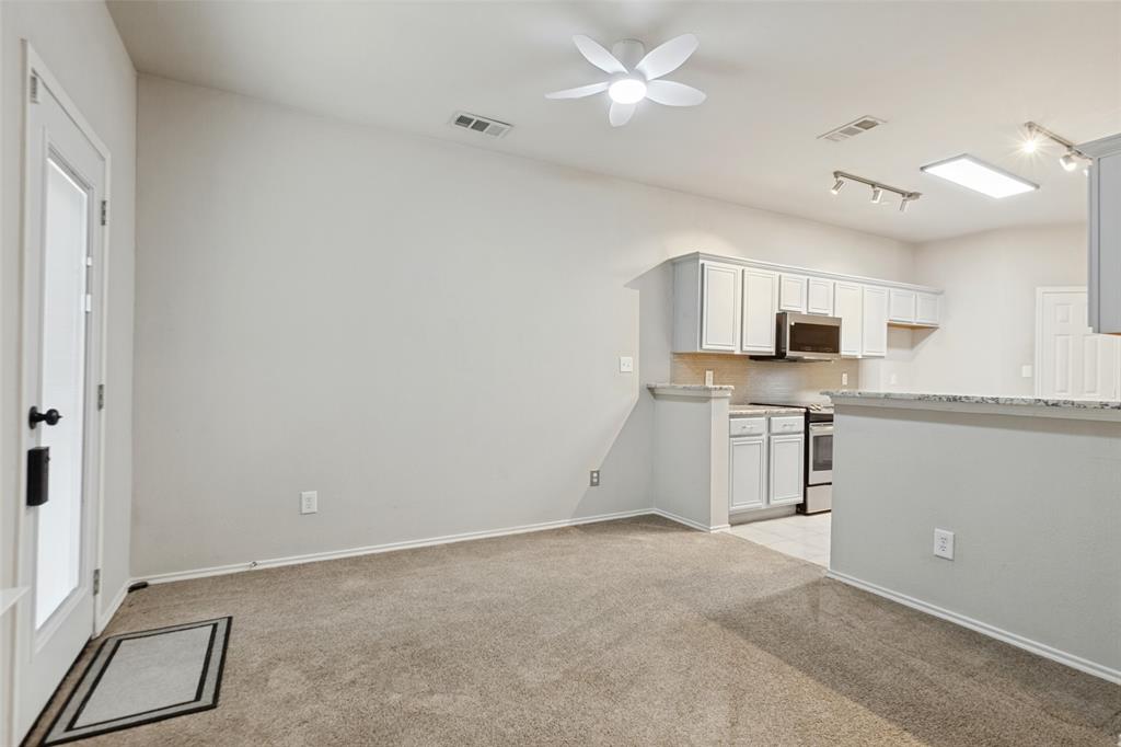 Open-concept kitchen area featuring white shaker-style cabinetry, stone-patterned countertops, a stainless steel built-in microwave, track lighting, and a multi-blade ceiling fan