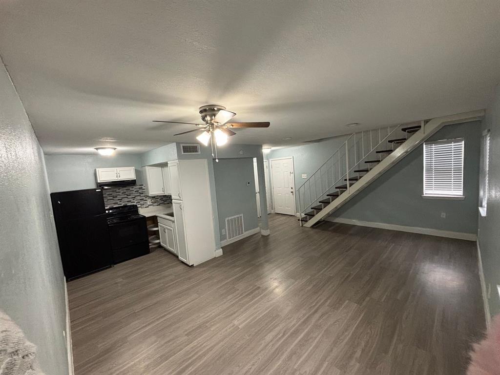 Kitchen featuring white cabinetry, patterned backsplash, and built-in appliances, accented by wood-finish flooring and an architectural staircase