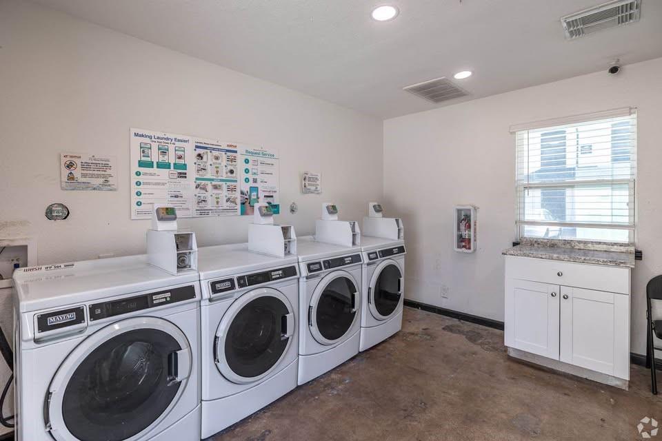 Shared laundry facility featuring four front-loading washers, a white cabinetry unit with a stone-finish countertop, and recessed ceiling lighting