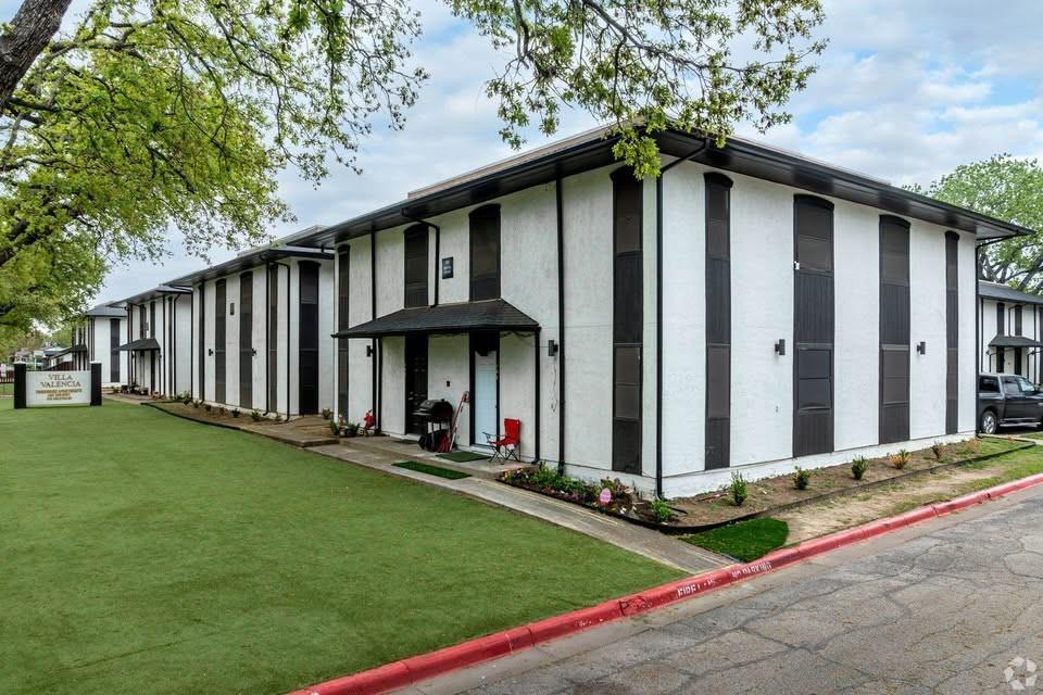 Two-story exterior featuring white stucco siding, dark vertical accent panels, overhanging gabled entry covers, and exterior wall-mounted light fixtures