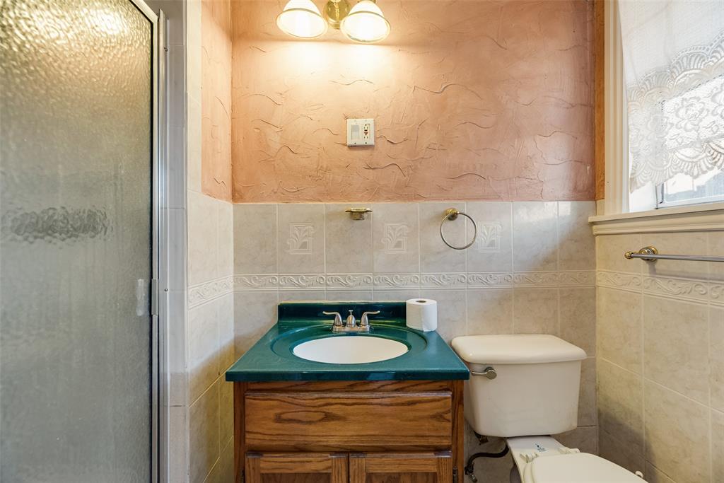 Bathroom featuring a wood-finish vanity with an integrated basin, textured wall finishes, a tiled backsplash with decorative inlay, and a glass-enclosed shower