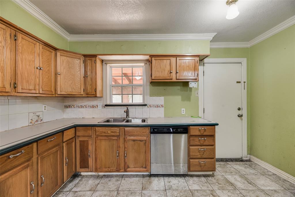 Kitchen featuring natural wood cabinetry, stainless steel dishwasher, dual-basin stainless steel sink, tiled backsplash, and stone-finish floor tiling