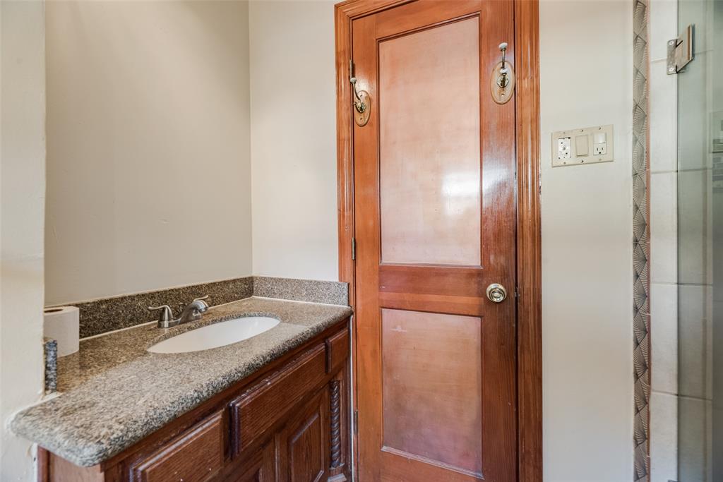 Vanity featuring a stone countertop with an integrated undermount sink, classic wood cabinetry, and an inset-panel solid wood door with brass-finish hardware