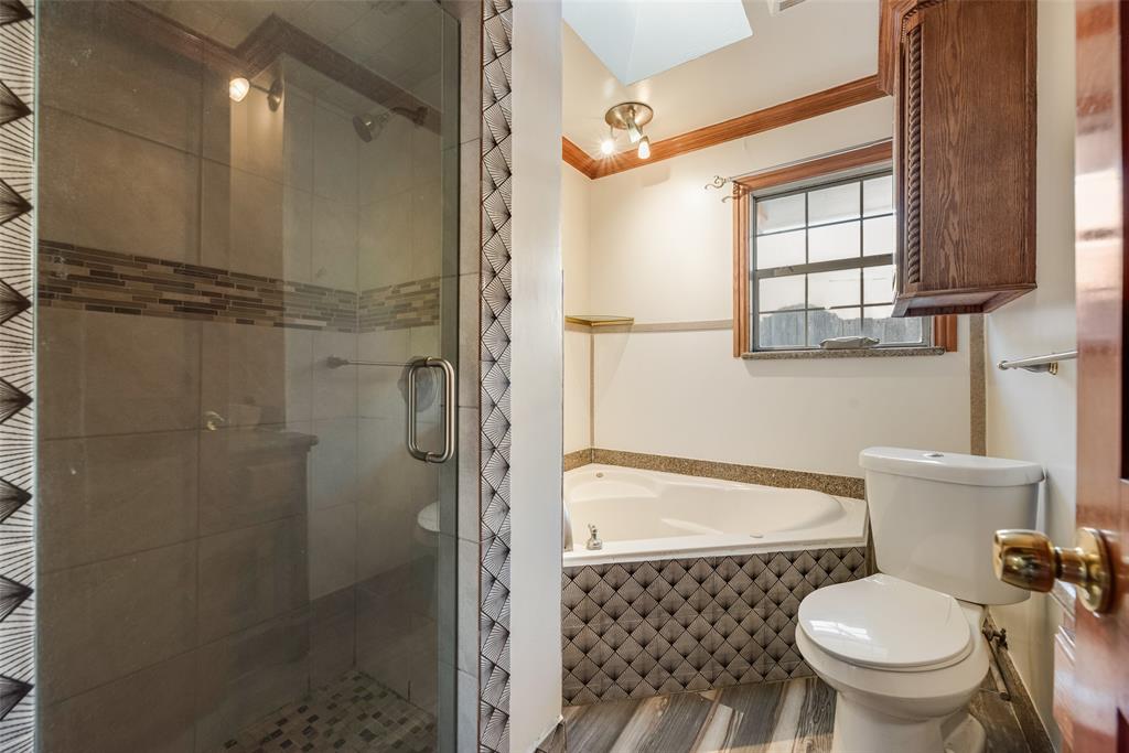 Bathroom featuring a glass-enclosed shower with a decorative tile inlay, a corner soaking tub with a patterned tile surround, and built-in wood-finish cabinetry