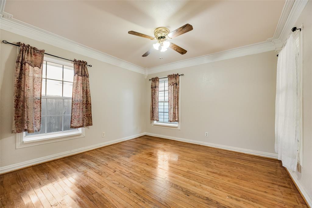 Room featuring wood-finish flooring, crown molding, and a ceiling fan with integrated lighting, accented by two windows with multi-pane glass