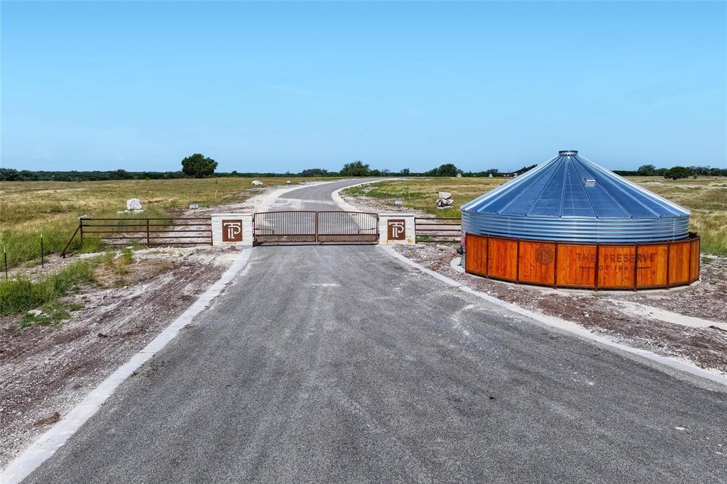 Gated entrance featuring masonry pillars, metal security gate, paved driveway, and custom circular water storage structure with wood-finish siding and metal roofing
