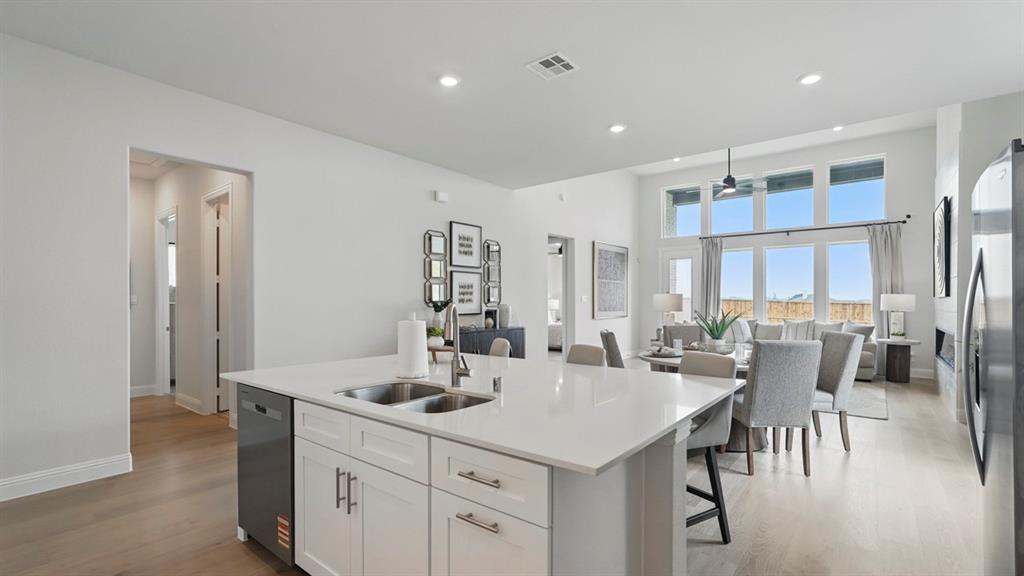 Kitchen island with a solid surface countertop, double-basin undermount sink, white shaker-style cabinetry, recessed ceiling lighting, and expansive multi-pane windows