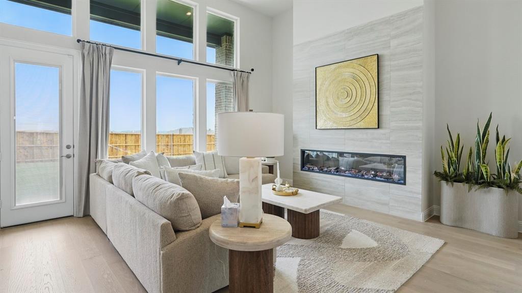 Living space featuring high ceilings, large multi-pane windows, wood-finish flooring, and a linear fireplace with floor-to-ceiling tile surround