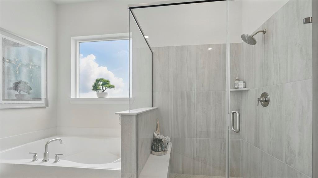 Soaking tub with chrome faucet, glass-enclosed shower featuring large-format tile surround, integrated shower shelving, and natural lighting from a window