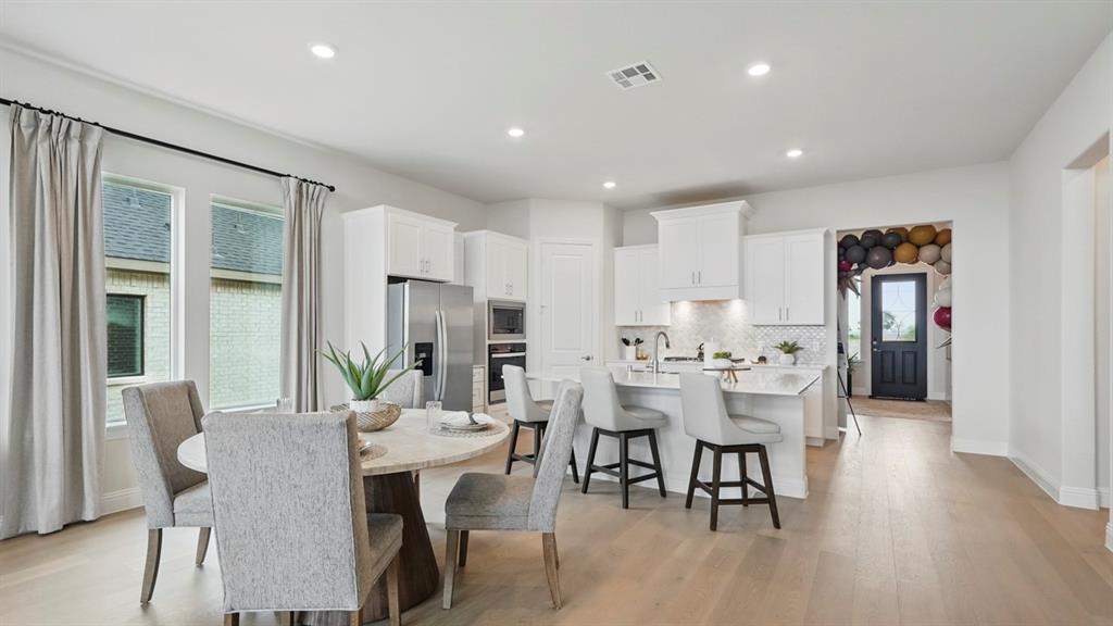 Open-concept kitchen featuring white cabinetry, a center island with stone-surface countertops, wood-finish flooring, and stainless steel appliances Open-concept kitchen featuring white cabinetry, a center island with stone-surface countertops, wood-finish flooring, and stainless steel appliances