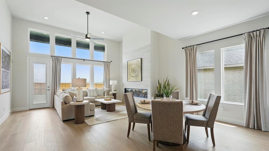 Open-concept living space with high ceilings, wood-finish flooring, floor-to-ceiling windows, and a built-in horizontal fireplace with stone surround Open-concept living space with high ceilings, wood-finish flooring, floor-to-ceiling windows, and a built-in horizontal fireplace with stone surround
