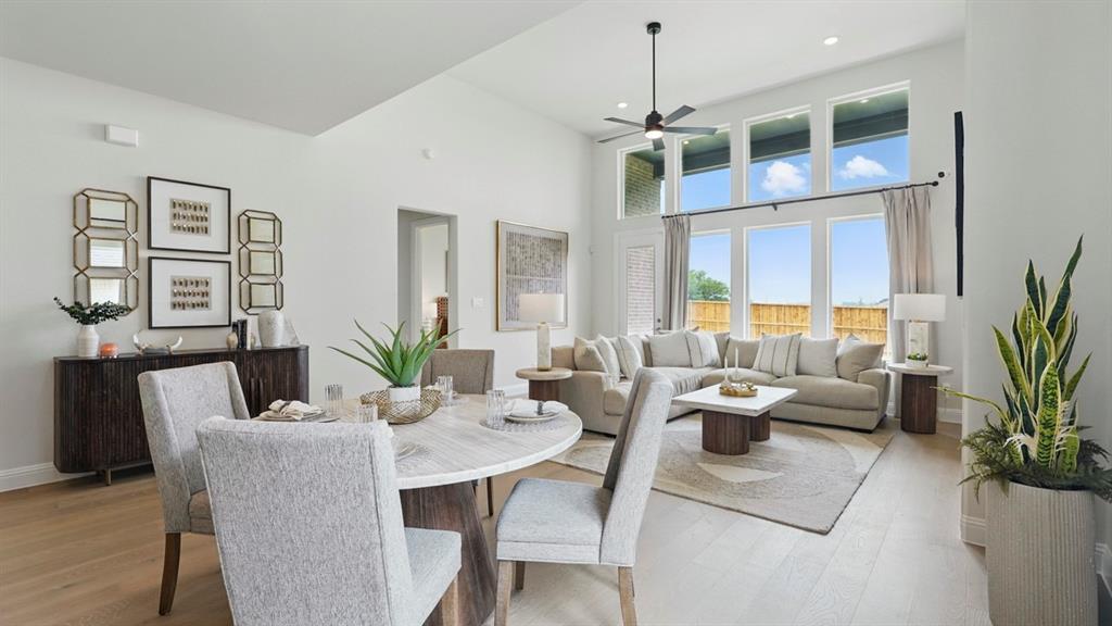 High-ceiling interior featuring a bank of tall windows, light wood-finish flooring, and a ceiling-mounted fan High-ceiling interior featuring a bank of tall windows, light wood-finish flooring, and a ceiling-mounted fan