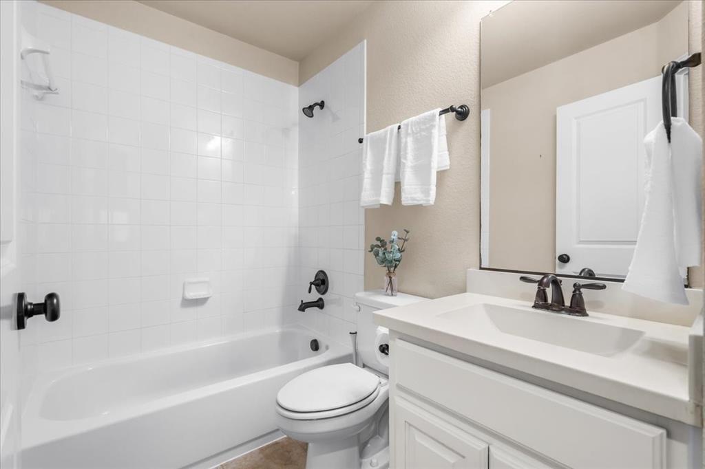 Bathroom featuring white tile shower surround, vanity with light-toned countertop, integrated rectangular sink, matte black hardware, and wall-mounted mirror
