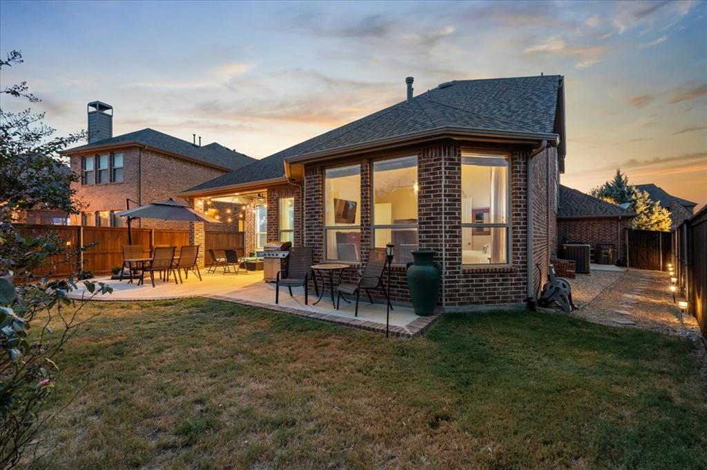Brick exterior rear elevation featuring a covered patio, extensive hardscaping, and large-format windows