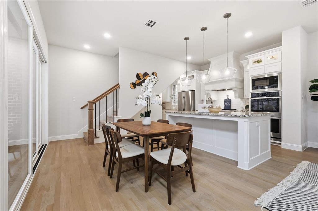 Kitchen featuring a center island, stainless steel wall-mounted double oven, custom white cabinetry, glass pendant lighting, and wood-finish flooring