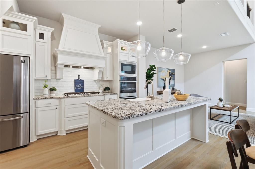 Kitchen featuring a central island with stone-finish countertops, white shaker-style cabinetry, custom range hood, stainless steel built-in appliances, and wood-finish flooring