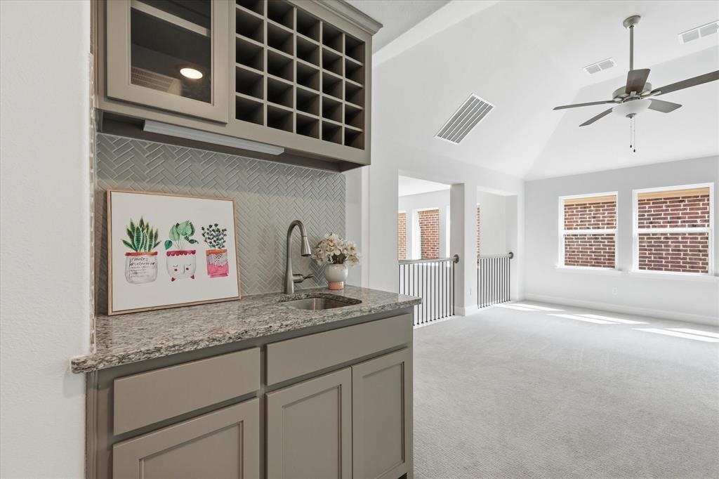 Built-in wet bar featuring stone-finish countertops, herringbone-pattern tile backsplash, glass-front cabinetry, and integrated wine storage