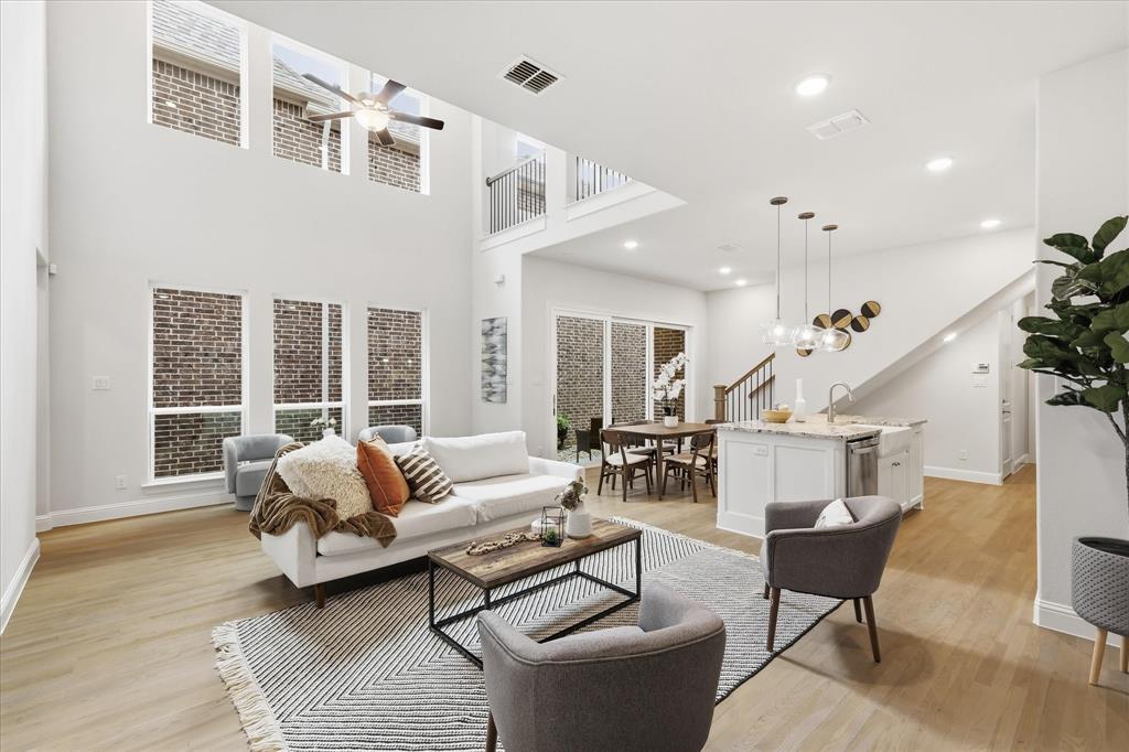Double-height living area featuring floor-to-ceiling windows, wood-finish flooring, recessed lighting, and a kitchen island with stone countertop