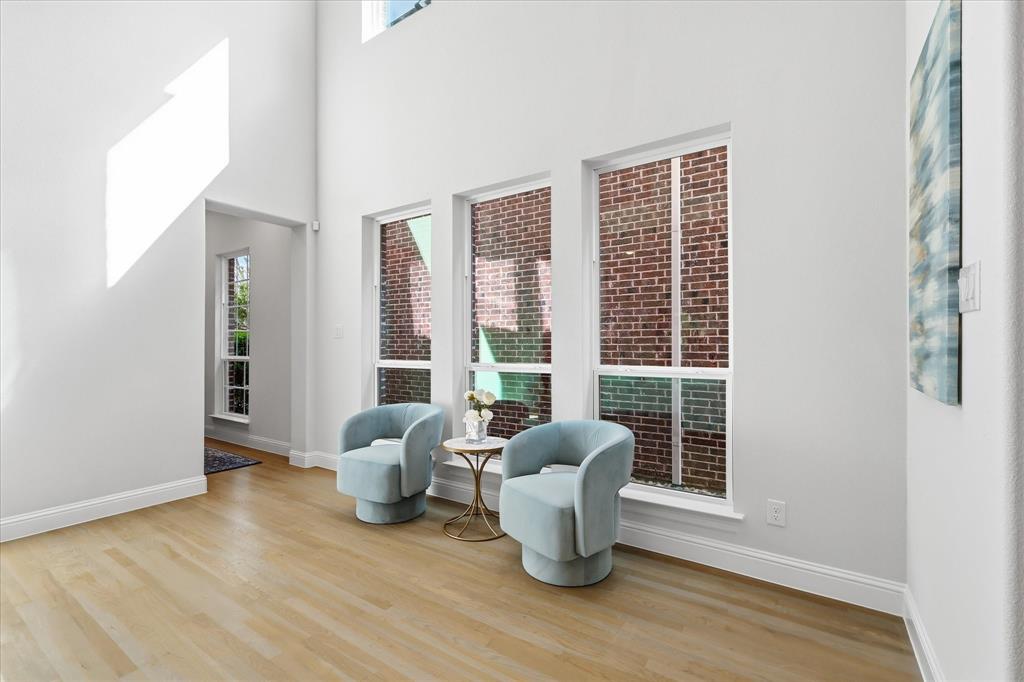 High-ceiling interior featuring wood-finish flooring, three vertical windows, and exposed exterior brick detailing