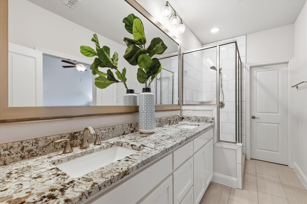 Dual-sink vanity with natural stone countertops, under-mount sinks, large-scale vanity mirror, and glass-enclosed shower with subway tile surround