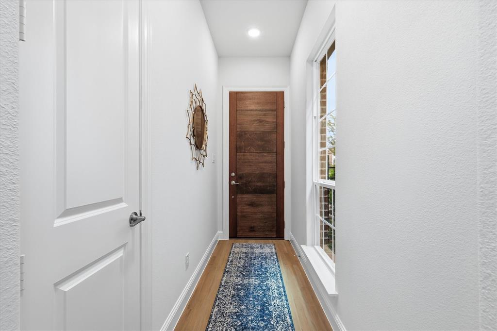 Wood-finish flooring, custom wood-grain door with brushed metallic hardware, recessed lighting, and a multi-pane window