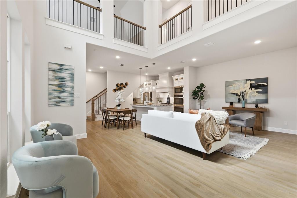 Double-height ceiling with an open mezzanine, wood-finish flooring, recessed lighting, and a staircase featuring a wooden handrail with metal balusters