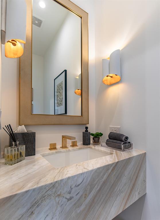 Floating vanity featuring stone countertop with integrated basin, wall-mounted metallic faucet, framed wall mirror, and dual structured sconce lighting