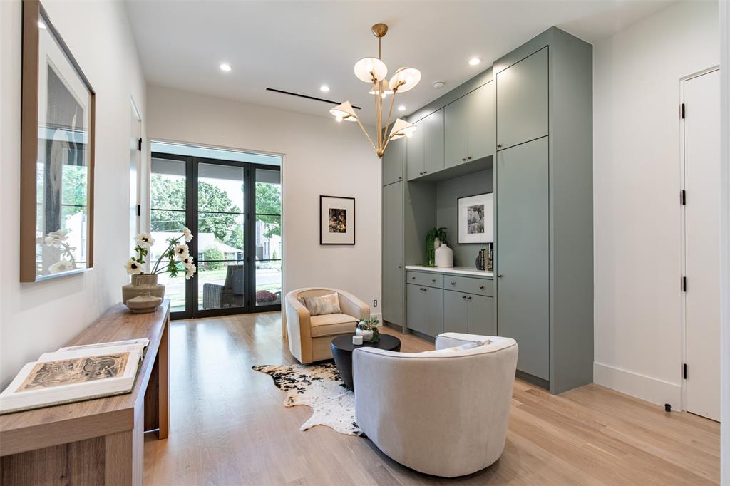 Custom sage-toned floor-to-ceiling cabinetry with built-in storage, light-toned wood-finish flooring, multi-light brass chandelier, and black-framed glass-paned doors