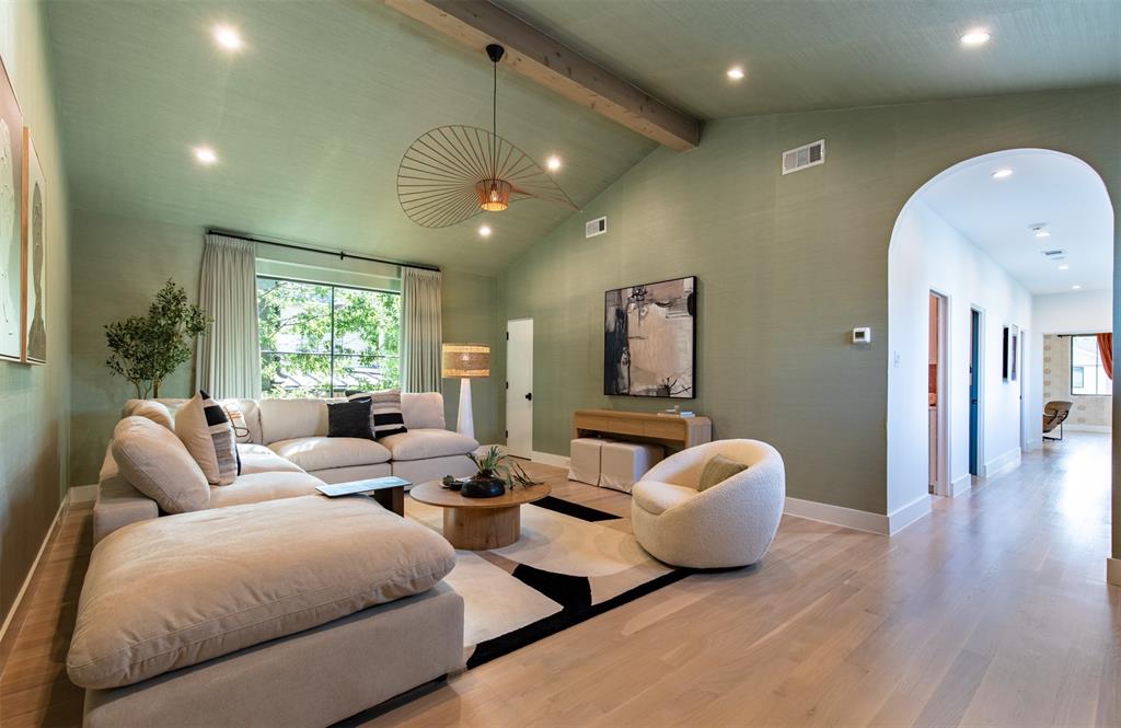 Vaulted ceiling featuring an exposed wood beam, recessed lighting, expansive picture window, arched entryway, and wide-plank wood-finish flooring