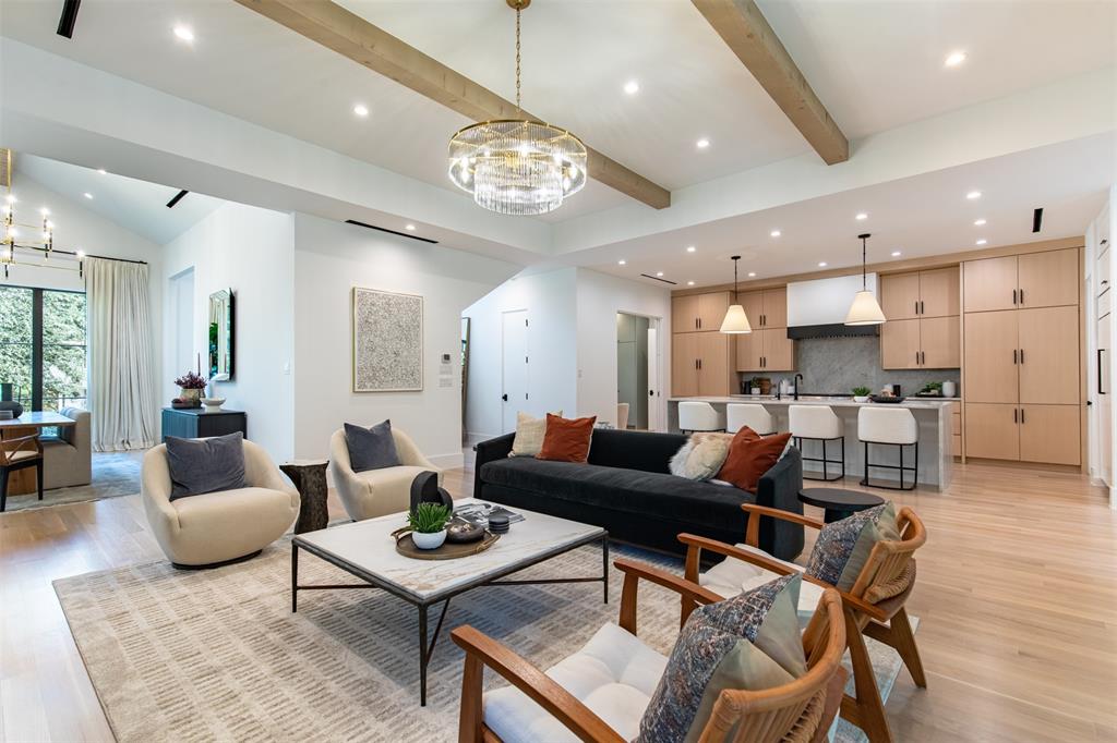 Open-concept living space featuring vaulted ceilings with exposed wood beams, recessed lighting, wood-finish flooring, a tiered crystal chandelier, and a kitchen equipped with light-toned cabinetry and a central island with pendant lighting
