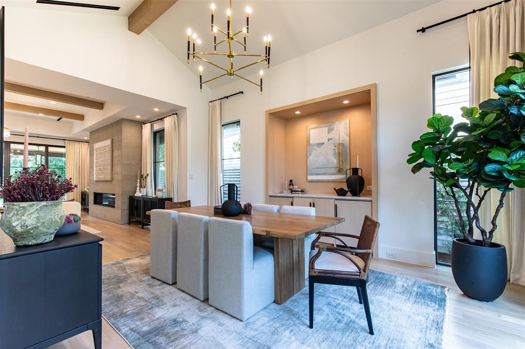 Vaulted ceiling with exposed wood beams, built-in recessed cabinetry, linear stone-finish fireplace, and multi-arm brass chandelier