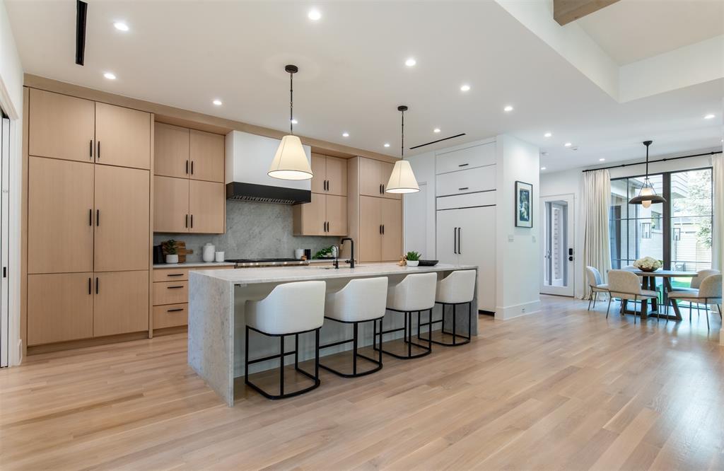 Kitchen featuring light wood-finish cabinetry, a waterfall-edge center island, stone-surround backsplash, recessed lighting, and wood-finish flooring