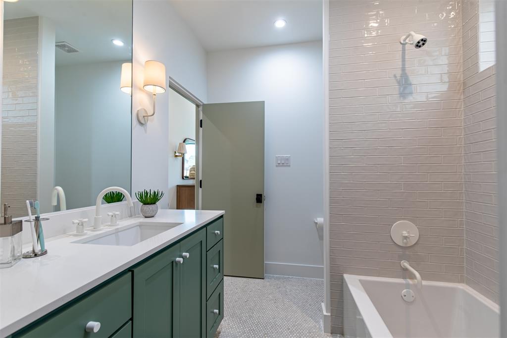 Bathroom featuring a green custom vanity with a white countertop, wall-mounted light fixtures, mosaic tile flooring, and a shower-tub combination with horizontal wall tiling