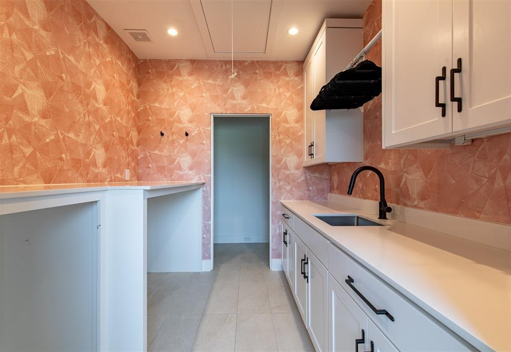 Laundry room featuring custom white cabinetry with matte black hardware, stone-finish countertops, an undermount sink with a high-arch faucet, and patterned wall covering