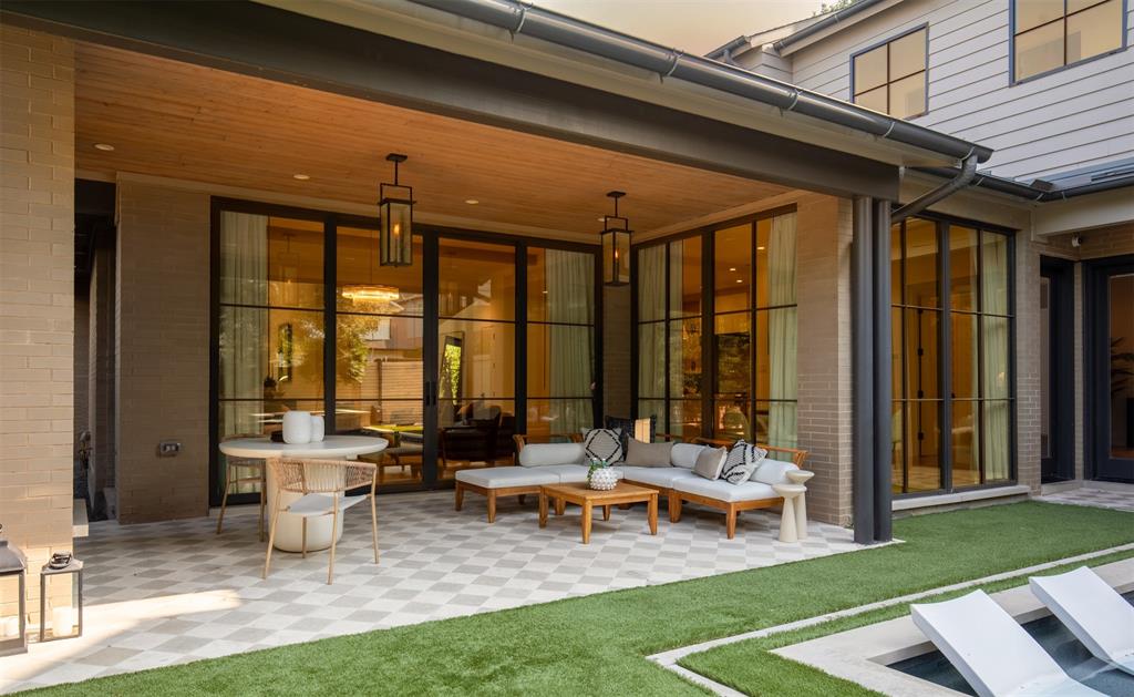 Covered patio featuring a wood-paneled ceiling, checkered stone flooring, black steel-frame glass doors, and suspended lantern-style lighting