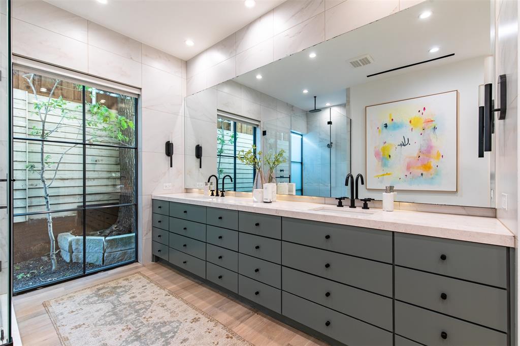 Dual-sink vanity featuring matte black fixtures, stone countertop, floor-to-ceiling mirror, and expansive wall-to-wall cabinetry