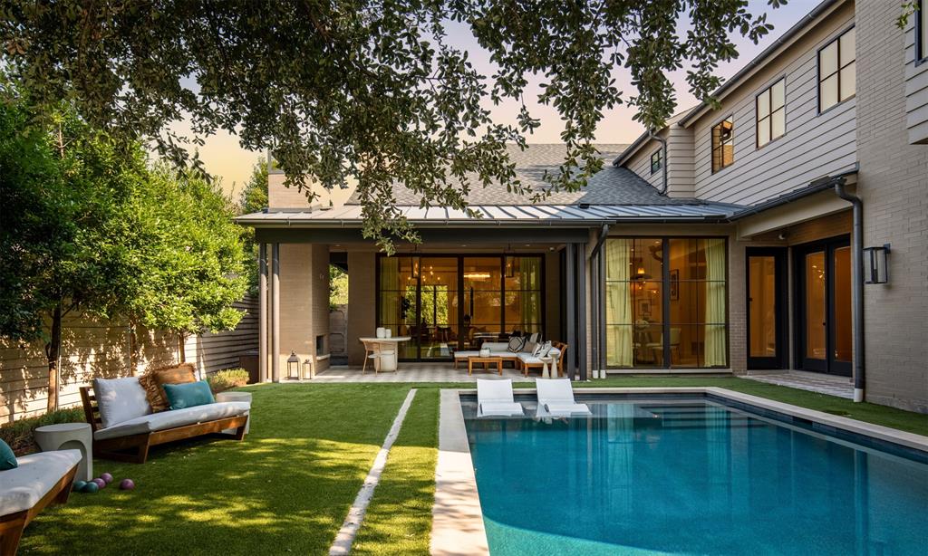Outdoor living space featuring a covered patio with metal roofing, an in-ground pool with a tanning ledge, expansive floor-to-ceiling glass panel doors, brick and horizontal siding exterior, and a manicured lawn